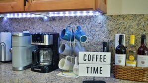 A kitchen counter with a coffee maker, mugs, and wine bottles.