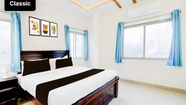 A classic hotel room with a large bed, a nightstand, a desk, and a window with curtains. - HOTEL GREENLANE SUITES (Hyderabad)