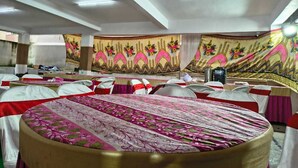 A banquet hall with round tables covered in pink and white tablecloths, chairs with red and white covers, and large floral wall tapestries. - HOTEL GREENLANE SUITES (Hyderabad)