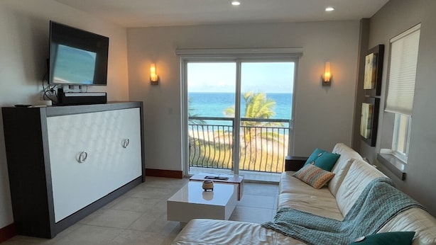 Un salon avec un canapé, une table basse, un téléviseur posé sur un meuble et un balcon offrant une vue sur l’océan.