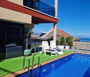 A rooftop pool area with lounge chairs, a small pool, and a view of the ocean.