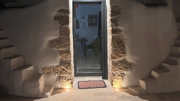 Un escalier en pierre mène à une porte dotée d’un panneau de verre, le tout étant encadré par un mur blanc.
