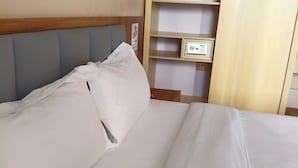 A neatly made bed with white linens, a wooden headboard, and a shelf unit with a small electronic device on it.