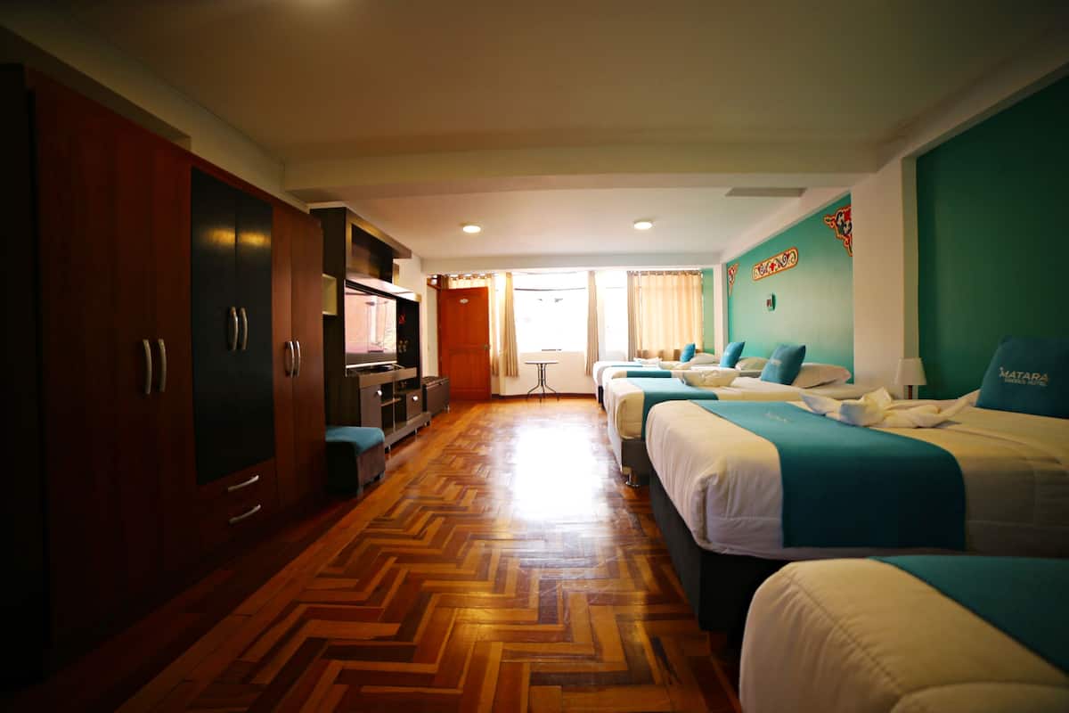 A hotel room with a wooden herringbone floor, two beds with matching headboards, a desk with a chair, a wardrobe, and a television.