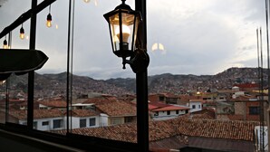 A view through a window with hanging light fixtures, overlooking a densely packed urban area with terracotta-roofed buildings. - Matara Green's Hotel (Cusco)