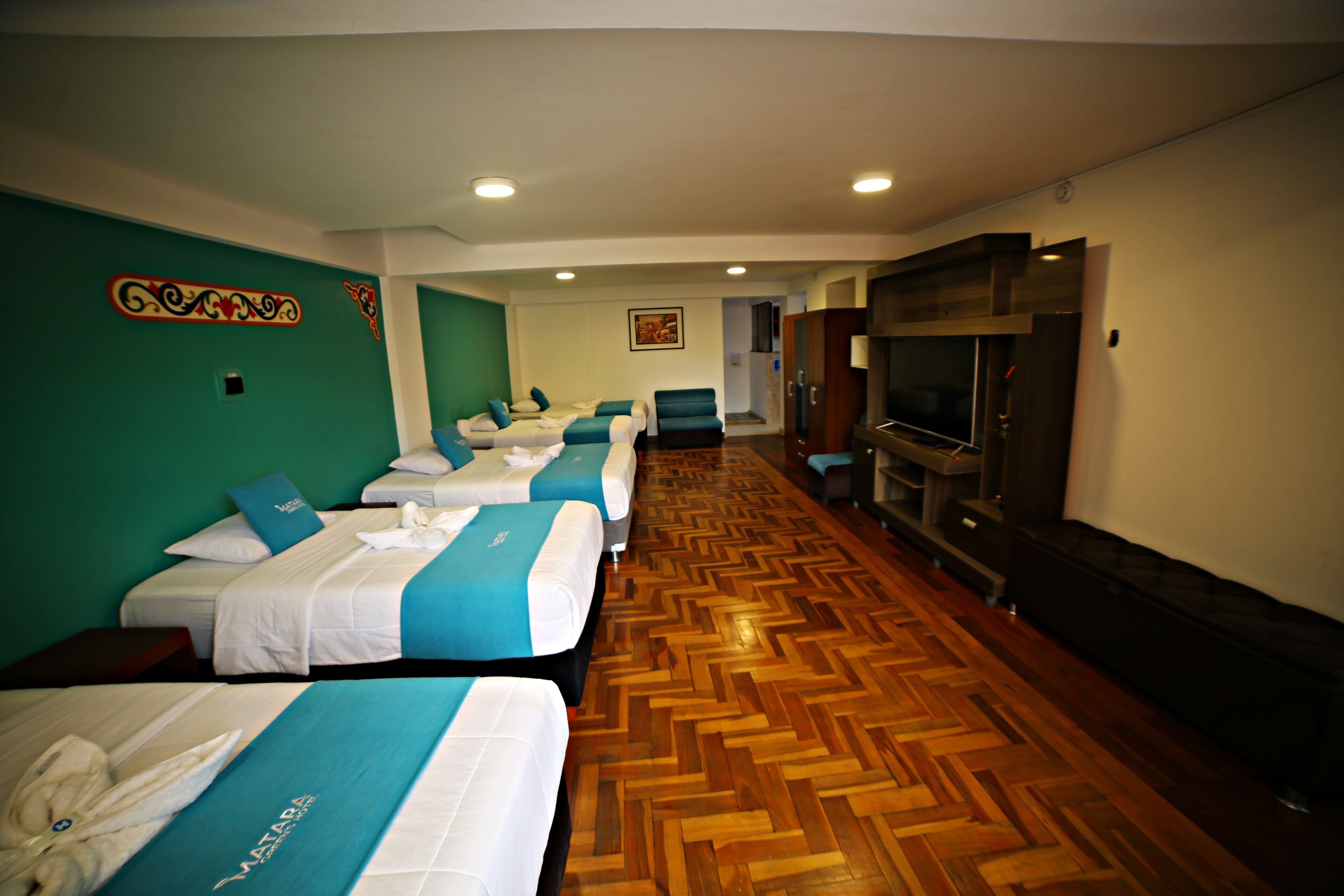 A hotel room with four beds aligned in a row, a television, and a wooden parquet floor.