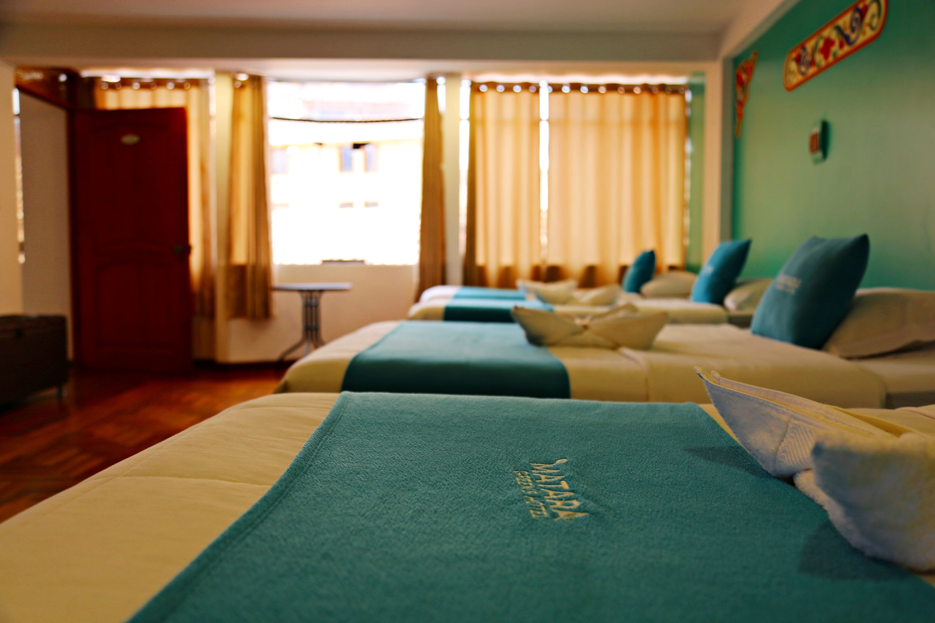 A hotel room with two beds, each with a blue bedspread and pillows. There is a small table and a chair in the room.