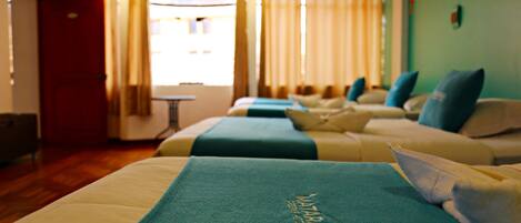 Habitación de hotel con dos camas, cada una con cubrecama y almohadas azules. Hay una mesita y una silla en la habitación.