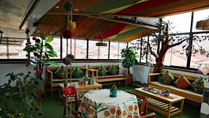 A cozy indoor seating area with wooden furniture, a table with a floral tablecloth, and various potted plants. - Matara Green's Hotel (Cusco)