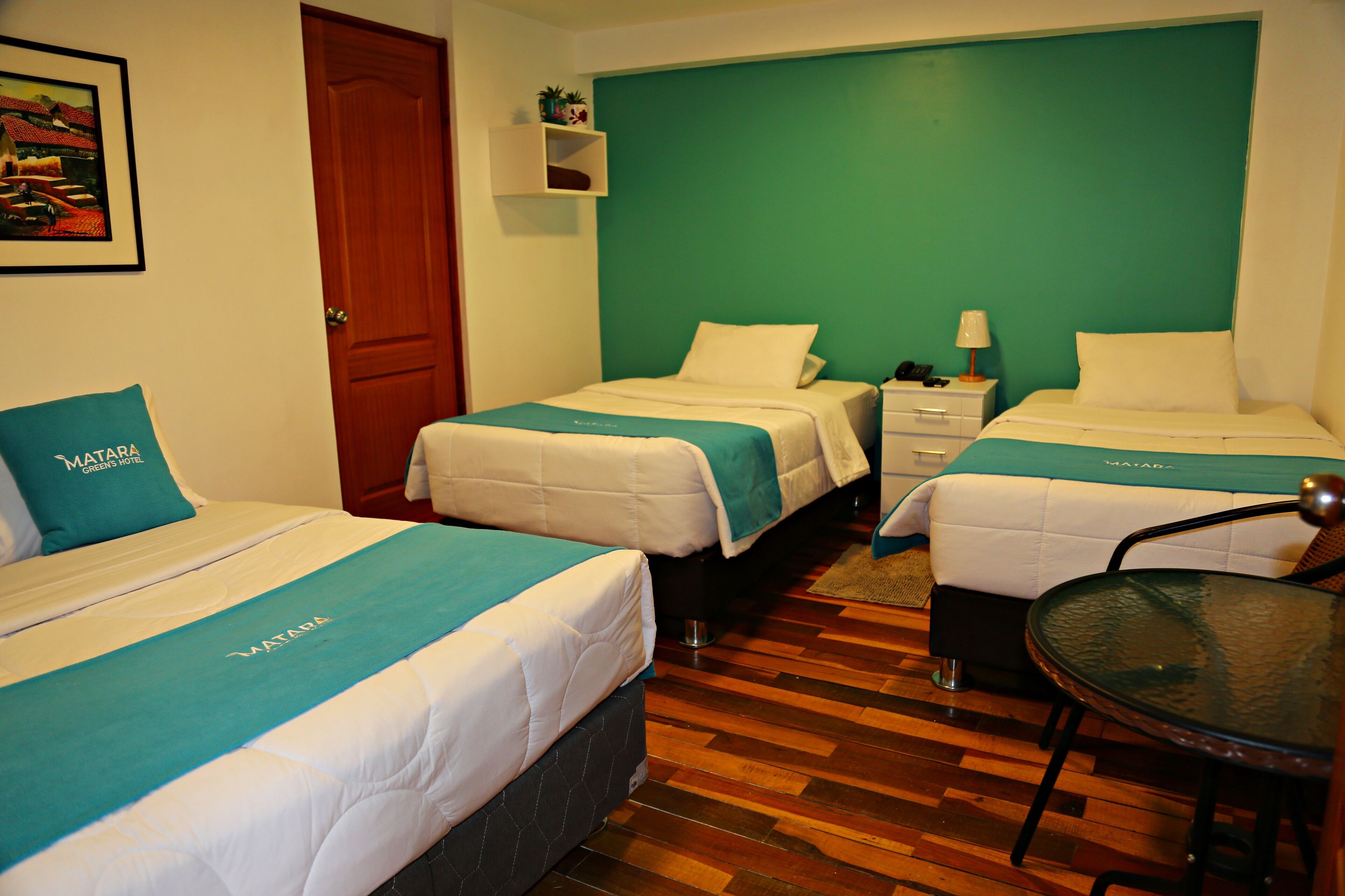 Habitación de hotel con dos camas, suelo de madera, una mesita y una mesita de noche con lámpara.