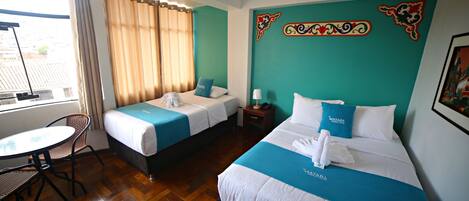 A hotel room with two beds, a small table, and a chair.