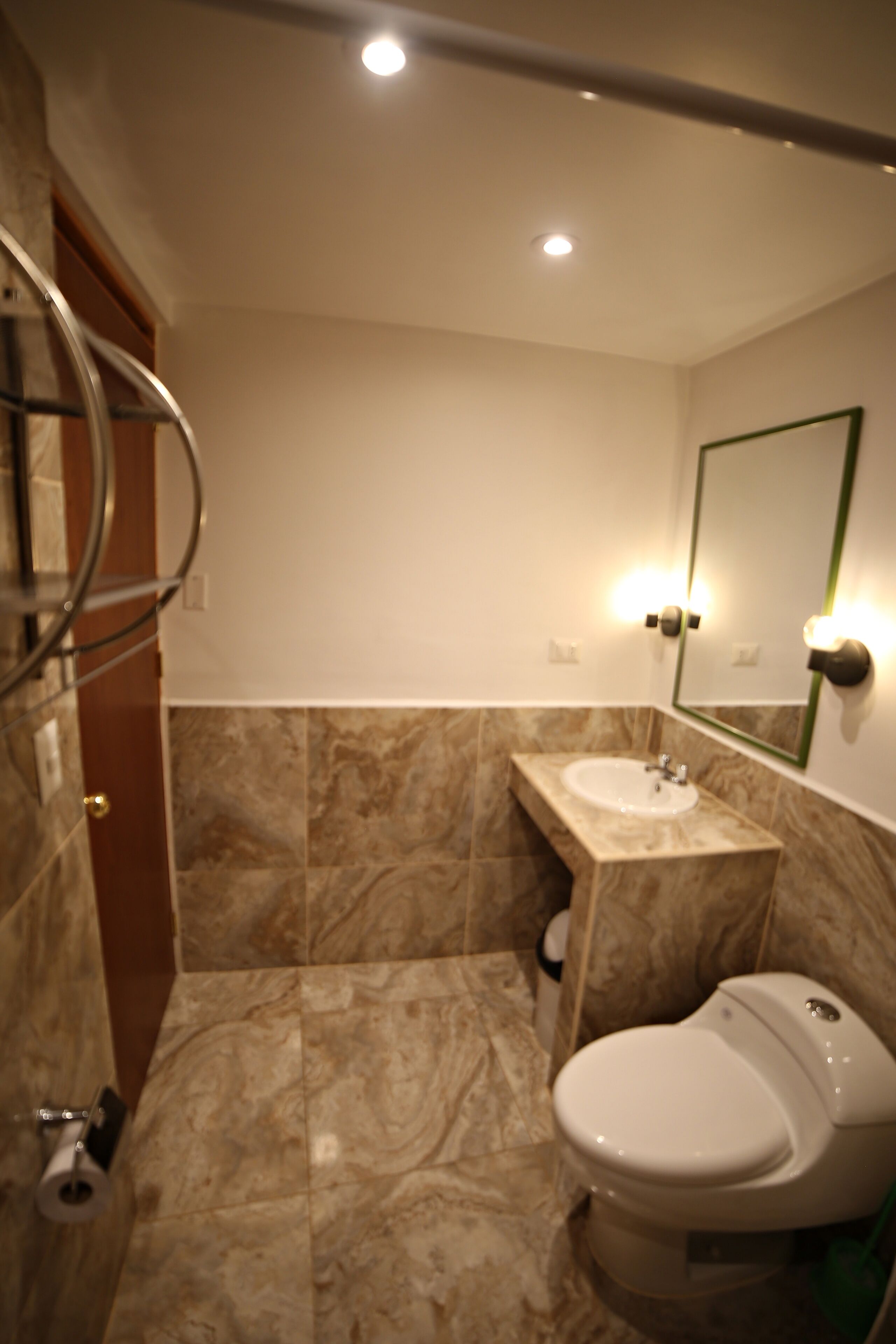 A bathroom with a marble floor, a sink, a toilet, and a mirror with lights.