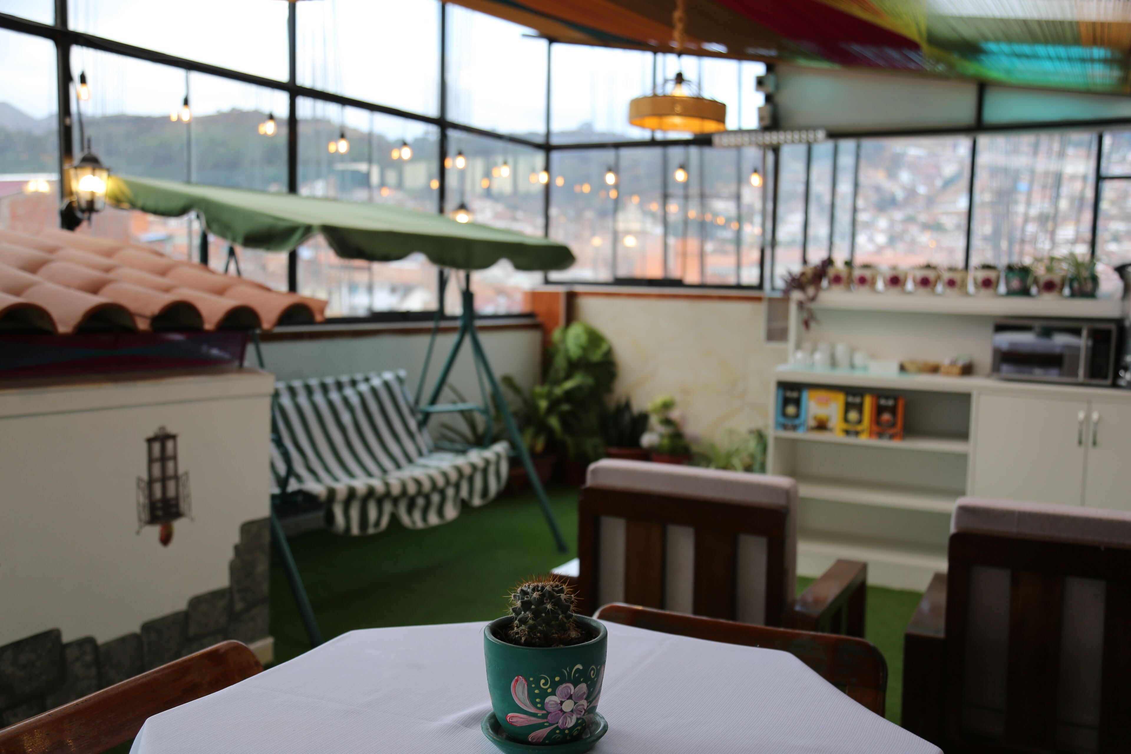 A cozy patio area with a table, chairs, a small cactus plant, and a view of the city through large windows.