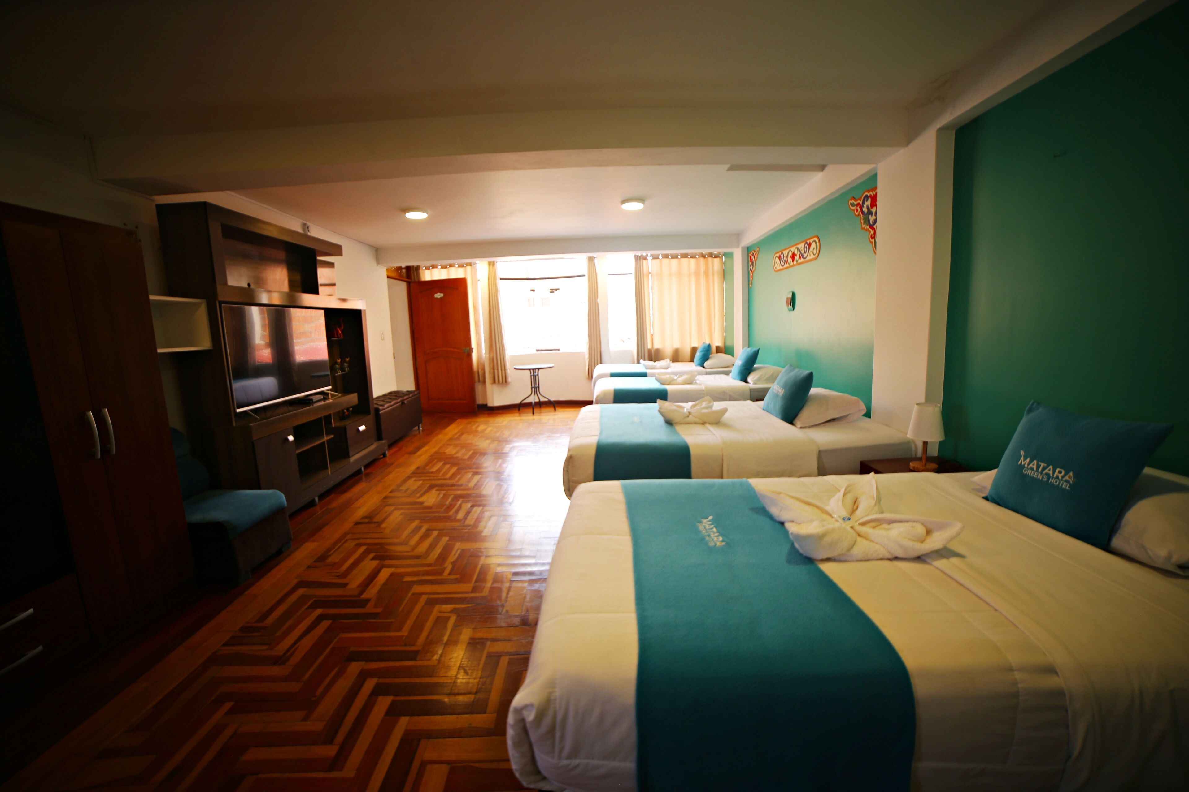 Habitación de hotel con dos camas, televisión, minibar y suelo de madera con diseño espiga.