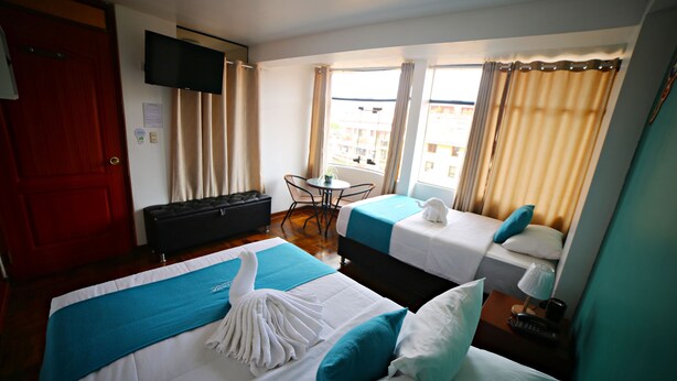 A hotel room with two beds, a TV, a small table, and a window with curtains. - Matara Green's Hotel (Cusco)