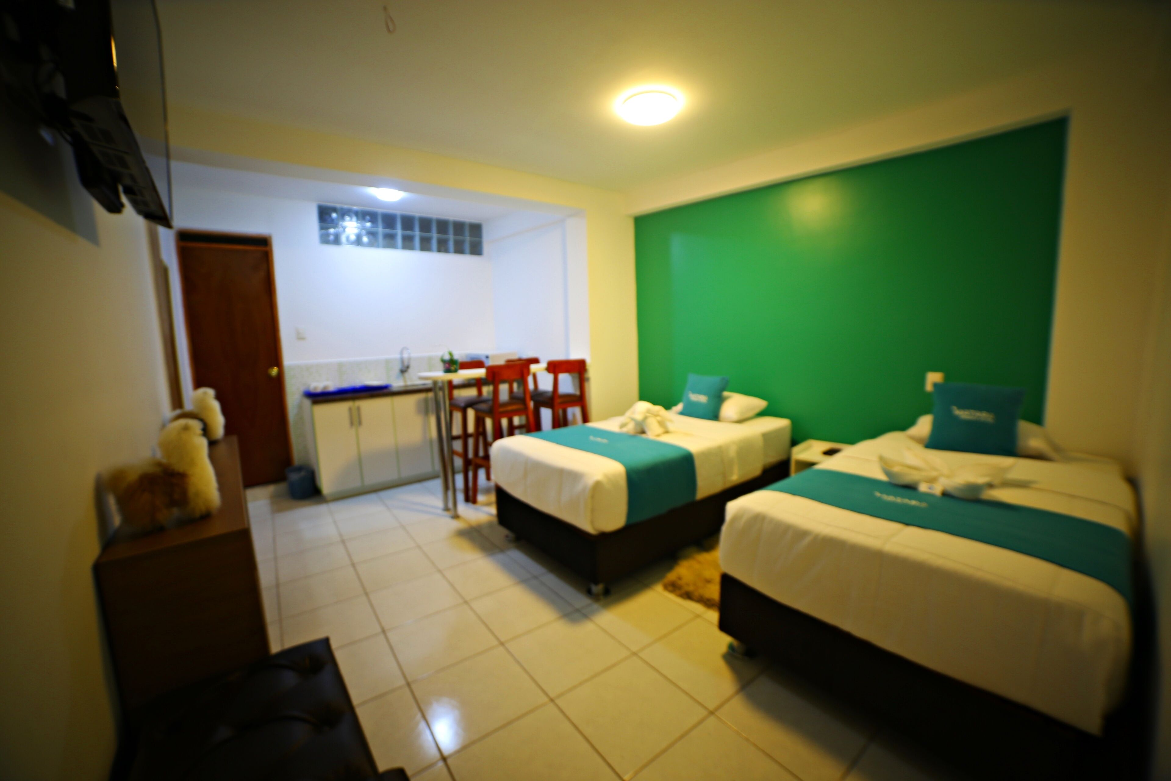 A hotel room with two beds, a kitchenette, and a green accent wall.