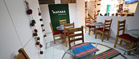 Habitación de hotel con una mesa redonda de vidrio, sillas de madera y una pared verde con el letrero 'MATARA Greens Hotel'.