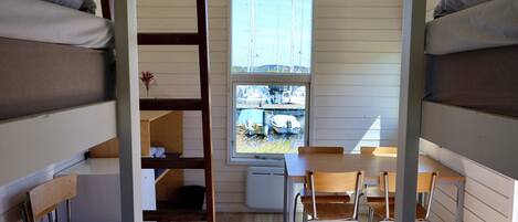 A dormitory room with bunk beds, a wooden desk, and chairs.