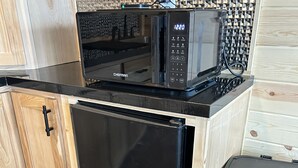 Eine kleine Küche mit einem schwarzen Kühlschrank, einer Mikrowelle und einem Mülleimer.