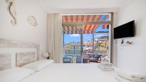 A hotel room with a large bed, a TV mounted on the wall, and a balcony with a view of the city.