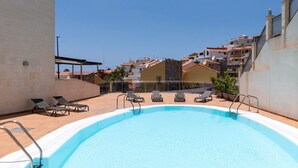 A rooftop swimming pool with lounge chairs and a clear view of surrounding buildings.