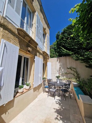 A courtyard with a table and chairs, potted plants, and a view of a building with shutters. - Magnificent town house with swimming pool in the heart of Provence (Salon-de-Provence)