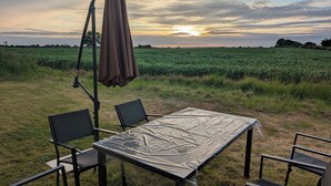Une table et des chaises installées à l’extérieur, dans un champ, avec un coucher de soleil en arrière-plan.