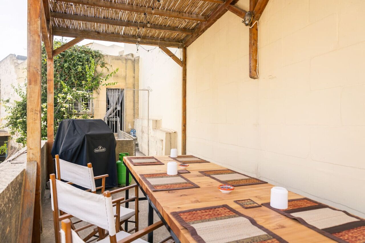 An outdoor patio with a wooden table, chairs, and a barbecue grill.