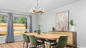 A dining area with a wooden table, green chairs, a chandelier, and a large abstract painting on the wall. - Dog Friendly! Hot Tub~Game Room~Fire Pit~3BR, 2BA~High Speed WIFI~8 Guests Max (Mount Hood Village)