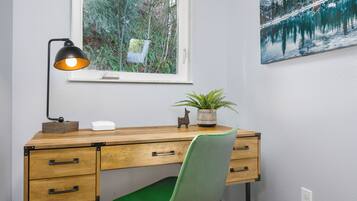 A wooden desk with drawers, a green chair, a desk lamp, a potted plant, and a window with a view of trees.