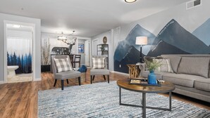 A modern living room with a grey sofa, two armchairs, a coffee table, and a wall mural depicting mountains. - Dog Friendly! Hot Tub~Game Room~Fire Pit~3BR, 2BA~High Speed WIFI~8 Guests Max (Mount Hood Village)