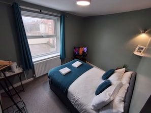 Habitación de hotel con cama, escritorio, televisor y ventana con cortinas.