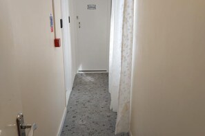 Un pasillo estrecho con alfombra estampada, una puerta con la leyenda 'Baño' y una cortina a la derecha.