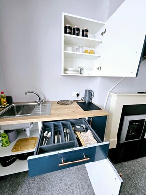 Una cocina compacta con un lavamanos empotrado, una encimera con hervidor y un armario de almacenamiento superior.