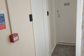 Un pasillo con una puerta que indica 'Baño' y una caja de alarma contra incendios en la pared.