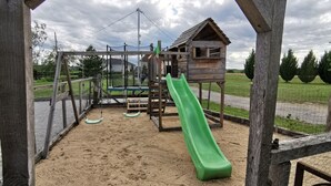 A playground with a green slide, swings, and a wooden climbing structure.