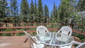 A wooden deck with a glass table and white chairs. - Cardinal Ridge (Big Bear City)