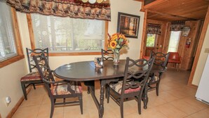 A dining area with a round table, six chairs, a vase with sunflowers, and a framed picture on the wall. - Cardinal Ridge (Big Bear City)
