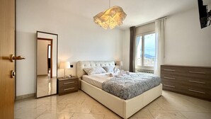 Un dormitorio moderno con una cama grande, mesitas de noche, un espejo y vistas de la ciudad a través de un amplio ventanal.