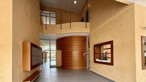 Un pasillo espacioso con una pared curva de madera, barandilla metálica en un nivel superior y una pequeña ventana con una planta.