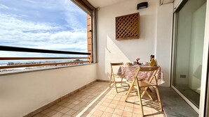 Un balcón con una mesa dispuesta para dos, un separador de madera con celosías y vistas al mar y a los edificios.
