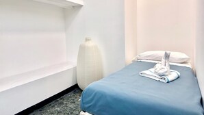 Ein Hotelzimmer mit einem Einzelbett, einer großen weißen Vase und einer blauen Bettdecke.