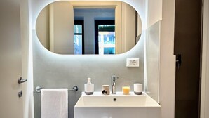 Ein Badezimmer mit Waschbecken, Spiegel, Handtuch, Seifenspender, Kerze und einem Glas Orangensaft.