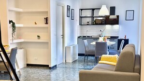 Ein modernes Wohnzimmer mit einer Couch, einem Esstisch mit Stühlen, einer Küchenzeile mit einer Mikrowelle und einer weißen Tür.