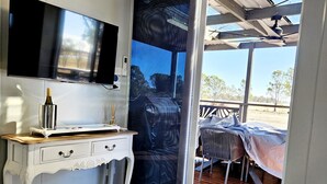 A room with a white vanity, a flat-screen TV mounted on the wall, and a sliding glass door leading to an outdoor seating area with a table and chairs.