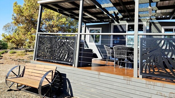 A modern building with a covered outdoor area, featuring a wooden deck and metal chairs.
