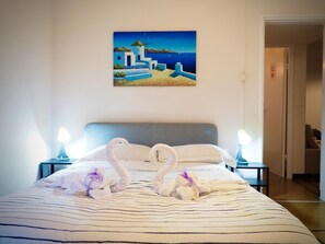A hotel room with a bed featuring a striped bedspread, two nightstands with lamps, and a painting of a coastal scene on the wall. - DIMORA DI SAN VINCENZO (BRIGNOLE) (GENOVA)