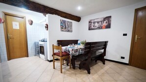 A dining area with a wooden bench and a table set for two, a kitchen with a stove, and a tiled floor. - Dimora S. M. di Castello (Aquarius) genovabnb it (GENOVA)