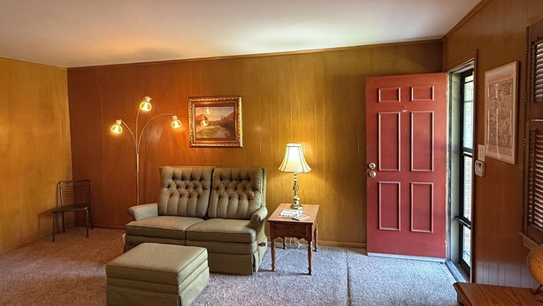Una habitación acogedora con un sofá capitonado, una mesita de noche con una lámpara, una puerta roja y un cuadro en la pared.