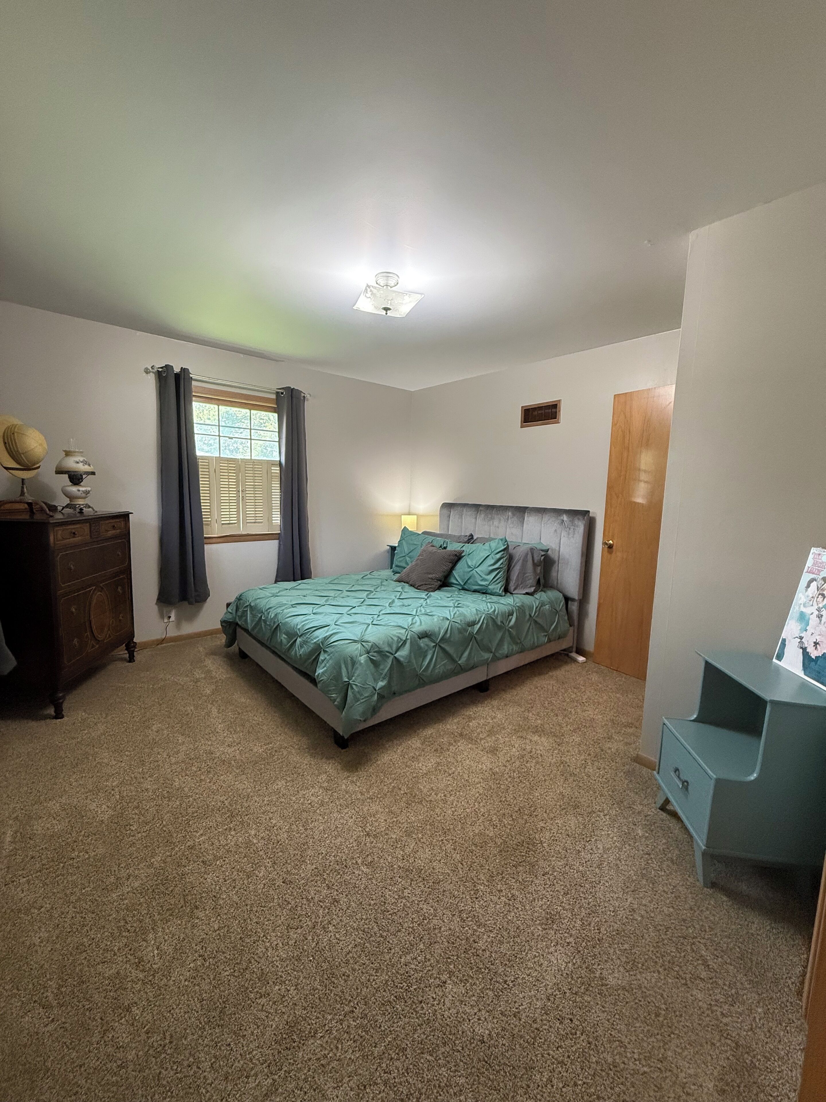 Un dormitorio con cama, cómoda, mesita de noche, ventana con cortinas y puerta.